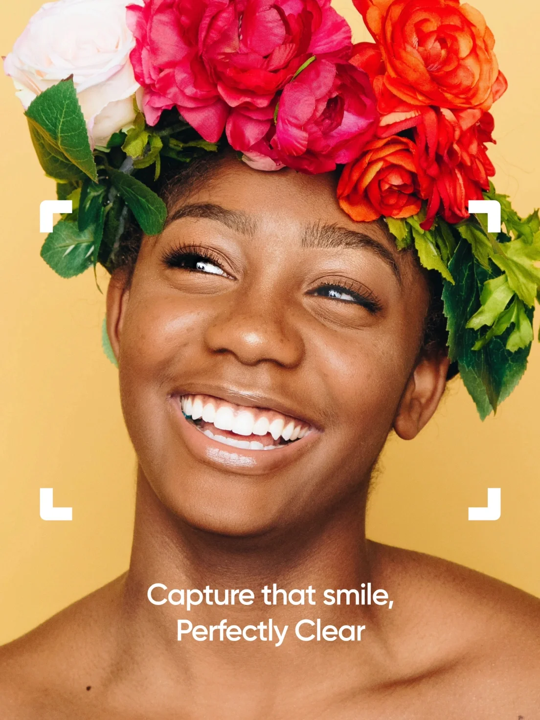 Smiling person with a colorful flower crown on yellow, framed by white corners. Perfectly Clear elevates your brand identity—capture that smile!