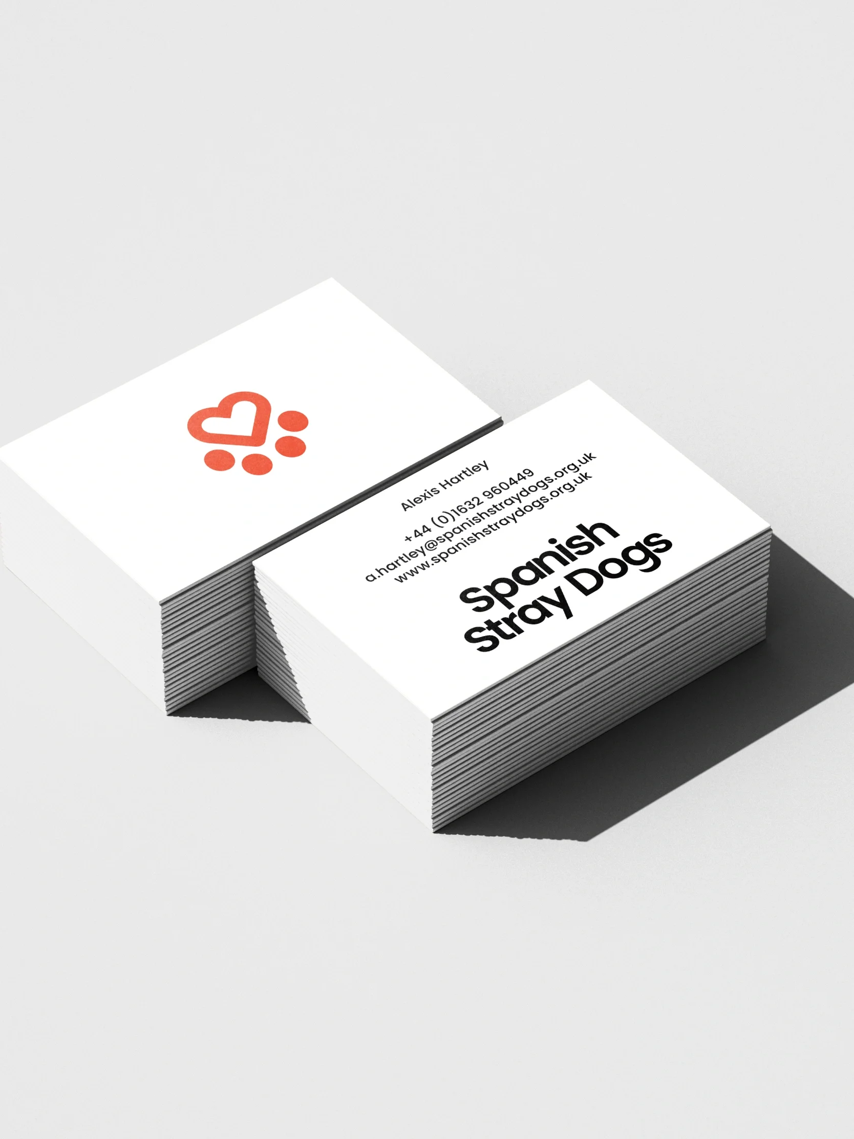 A stack of charity business cards with a red paw-heart logo, showcasing the Spanish Stray Dogs brand identity and contact details.