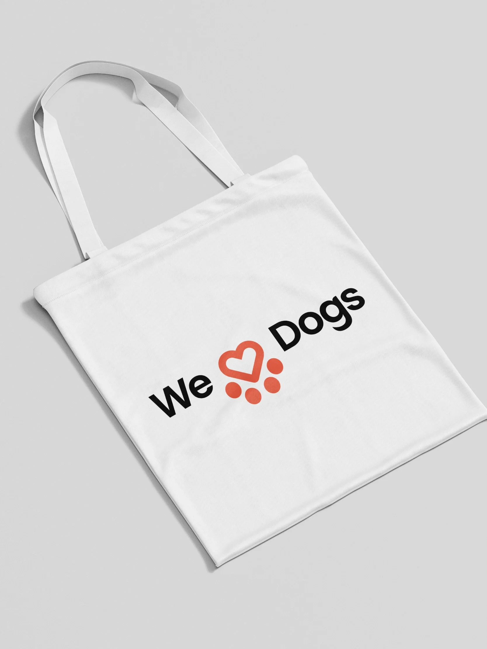 White tote bag with the text We love Dogs, heart made of paw prints; perfect for supporting Spanish Stray Dogs charity. Plain gray background.