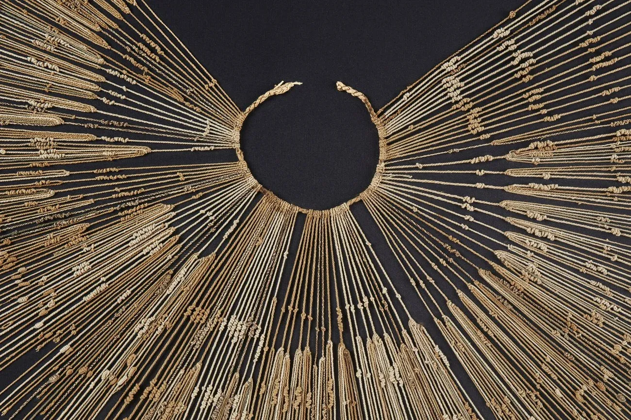 An Inca khipu photographed flat on a black background: a braided primary cord curves into an open ring at the centre, and more than a hundred pale twisted cotton pendant cords radiate outward from it like rays of a sun, each cord carrying its own clusters of knots tied at different heights.