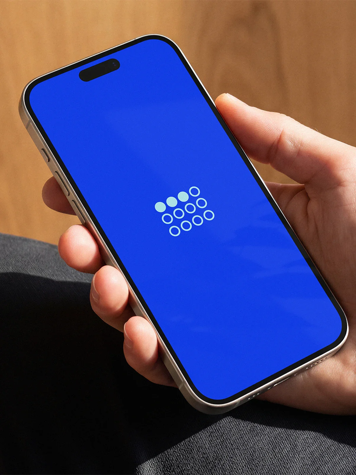 Hand holding a phone showing the Collectivally dot-grid logo on brand blue