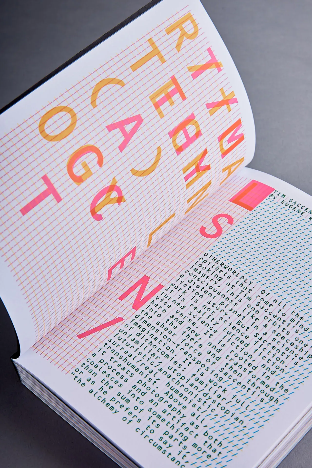 An open spread from Ritual Technology. The left page scatters large overlapping letterforms in fluorescent pink and warm orange across a fine printed grid, spelling fragments of the title. The right page carries an essay set in tall, narrow columns of green monospaced type rotated ninety degrees, over hatched cyan rules, beginning "Otherworldly: of all the epithets that come to mind looking at Tim Saccenti's imagery".